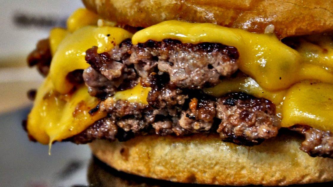 Doppelter Cheeseburger im Anschnitt: zwei Patties mit dunkler Kruste unter geschmolzenem Cheddar