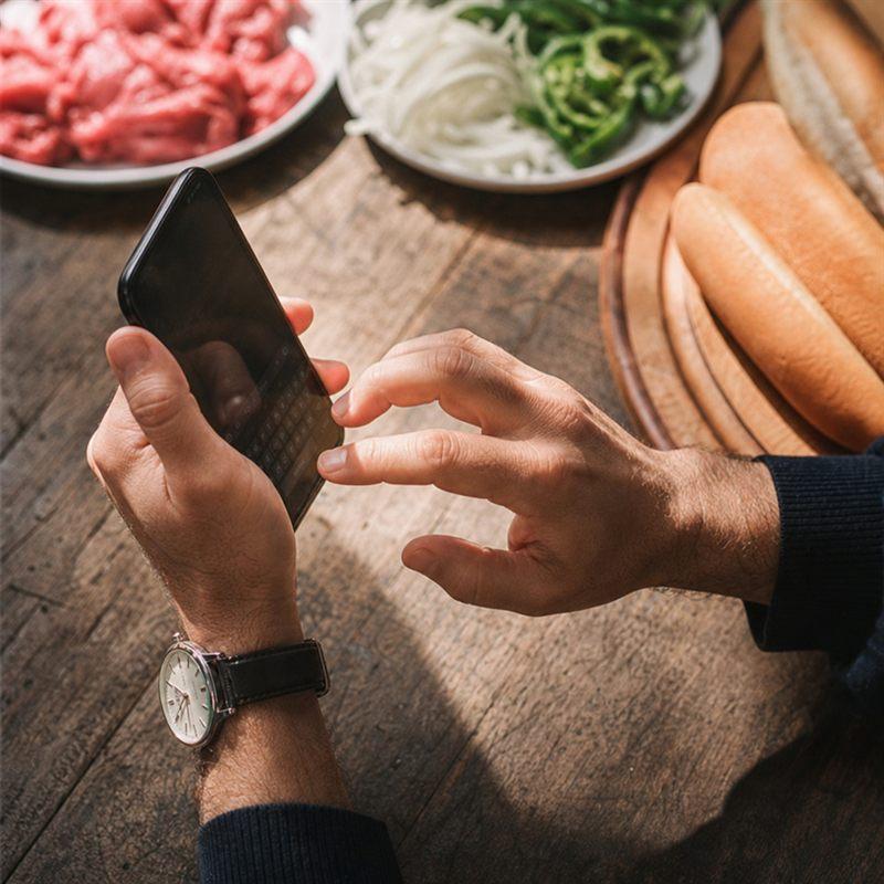 Hände tippen eine Anfrage am Smartphone, daneben frische Zutaten